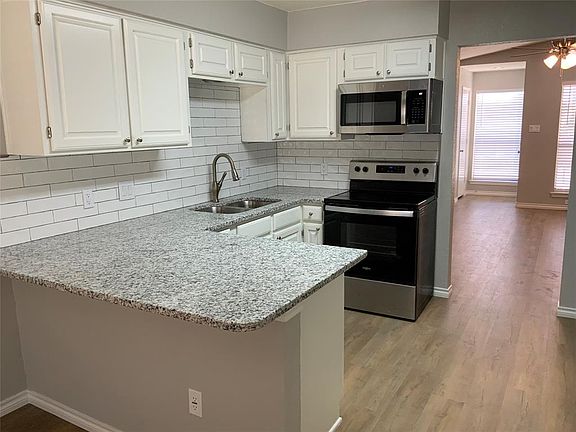 Kitchen with a sink, stainless steel appliances, a peninsula, and white cabinetry