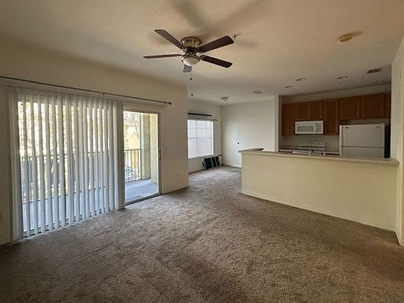 Spacious living room with high ceilings, working fan connected to kitchen that has a beautiful breakfast bar.