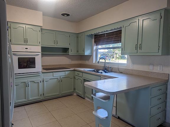 Kitchen with sink, bar area, wall oven, glass-top stove and refrigerator to the extreme left of photo.