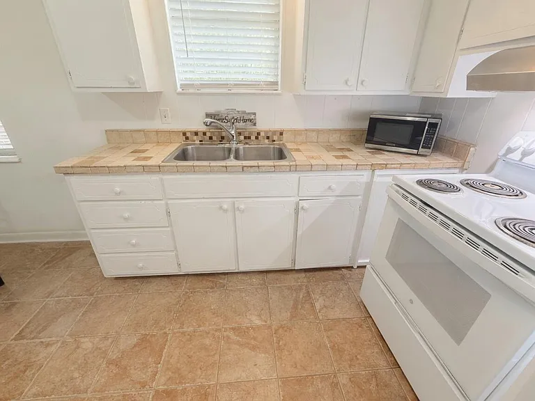 Functional kitchen with ample cabinet storage, tiled countertops, double-basin sink, and a full-size range for daily meals.