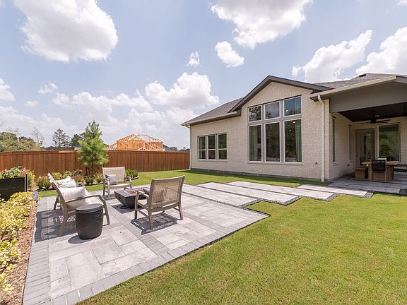 A modern, two-story house with a large patio and well-manicured lawn in the foreground, surrounded b