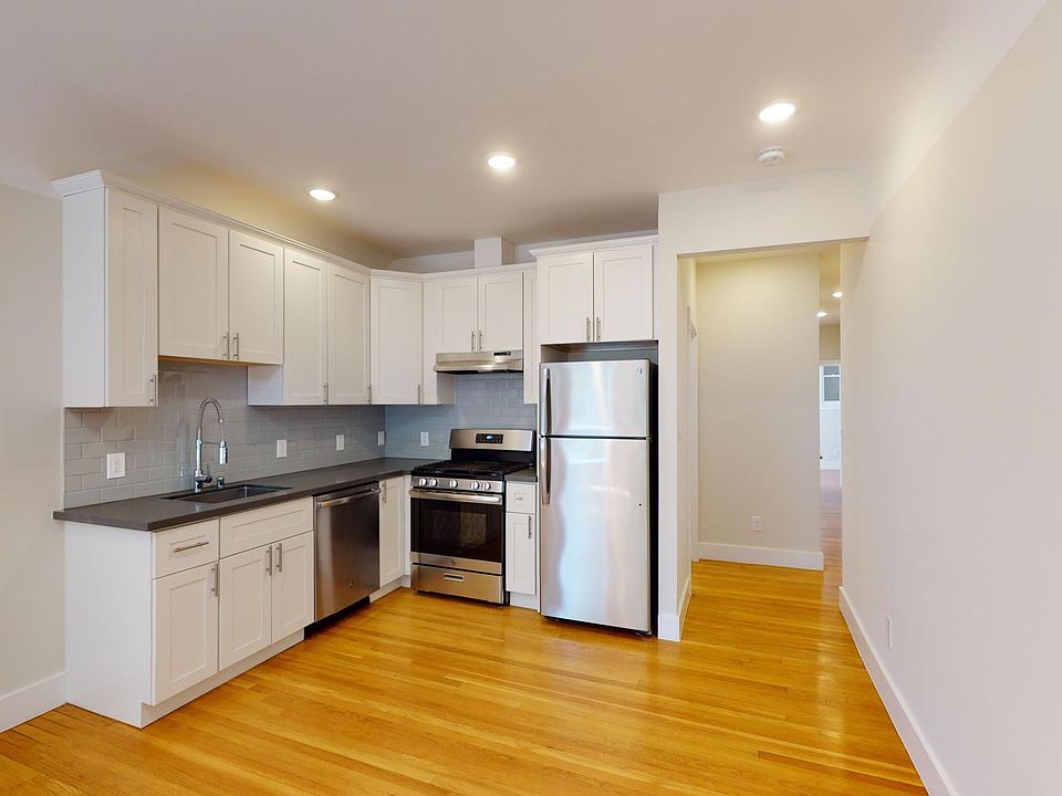 Kitchen with multiple cabinets, refrigerator, stove, range hood, and sink