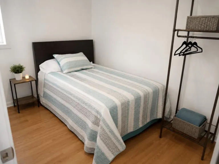 Furnished bedroom with twin bed, side table, and open garment rack on hardwood floors for easy everyday living.