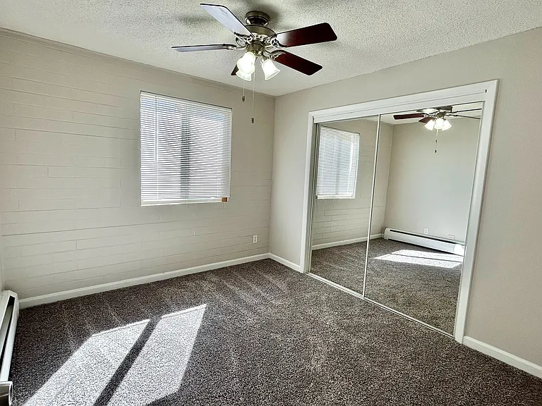 Bright bedroom with cozy carpet, mirrored closet doors, and ceiling fan, perfect for a relaxing retreat.