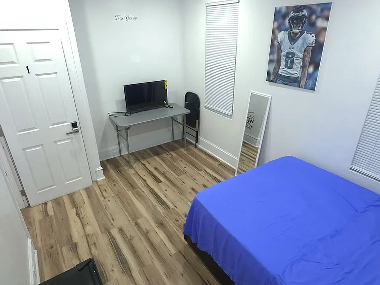 Private bedroom with wood-look flooring, two windows with blinds, and a workspace desk; includes a bed and floor mirror.