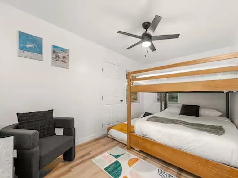 Bedroom with a queen-over-queen bunk bed and a twin trundle, sleeping up to 5 people. Includes a dedicated desk/vanity area and direct access to the sunroom for a seamless connection to the outdoor space.