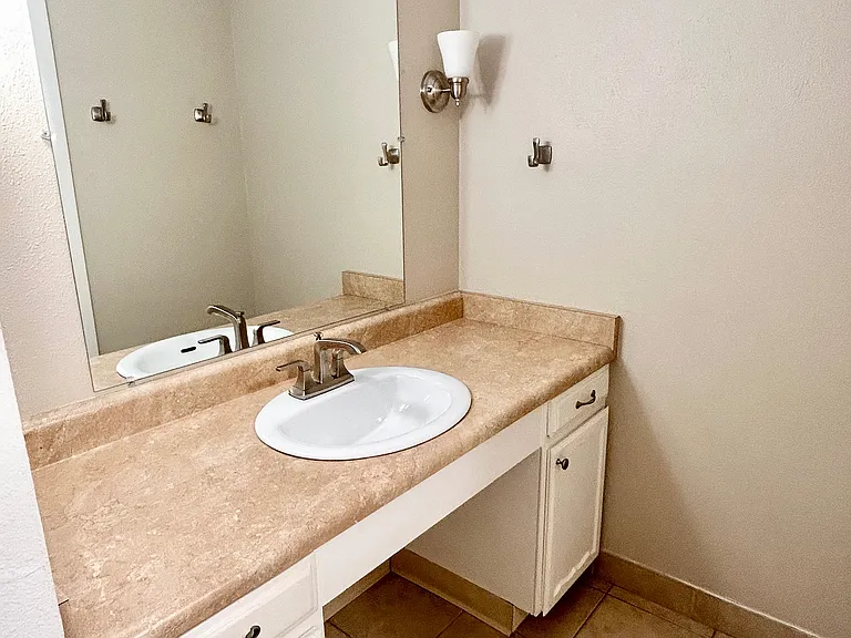 Modern bathroom with elegant beige countertop, sleek under-mount sink, and large wall mirror for a spacious feel.