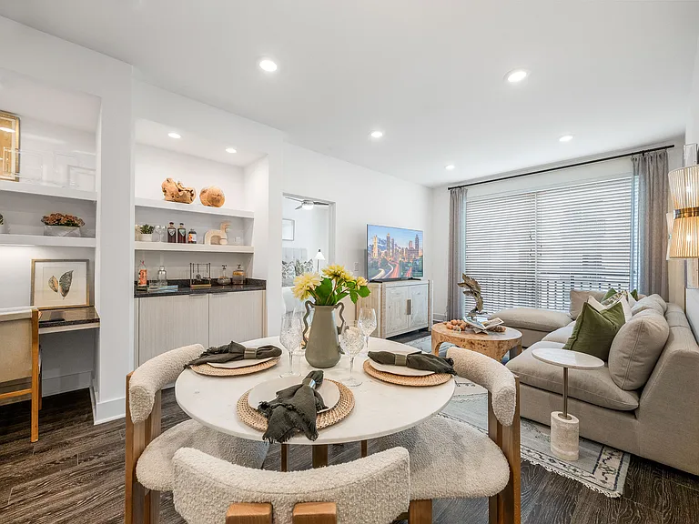 Contemporary living room with plush sofa, chic dining setup, and sleek shelving, accentuated by natural light from large windows.