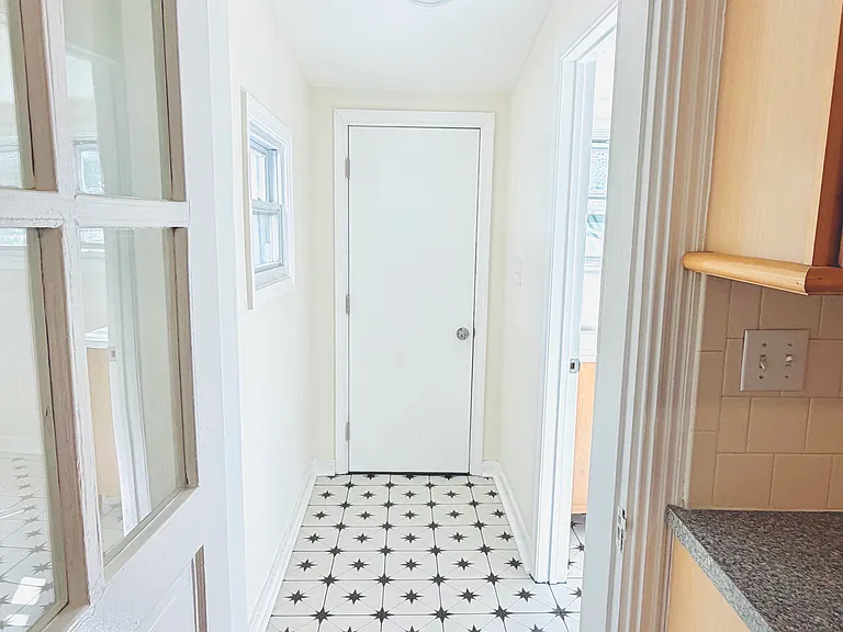 Hallway connecting kitchen to bathroom with eye-catching black and white star-pattern tile floor and glass-paned door.