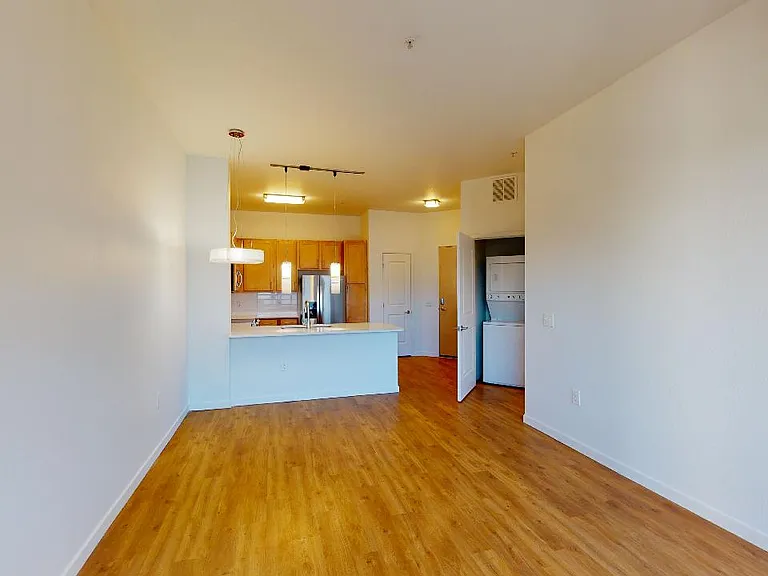 Apartment kitchen with stainless steel appliances, dining and living room with wood-style flooring.