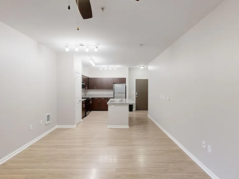 Apartment kitchen with stainless steel appliances, dining and living room with wood-style flooring.