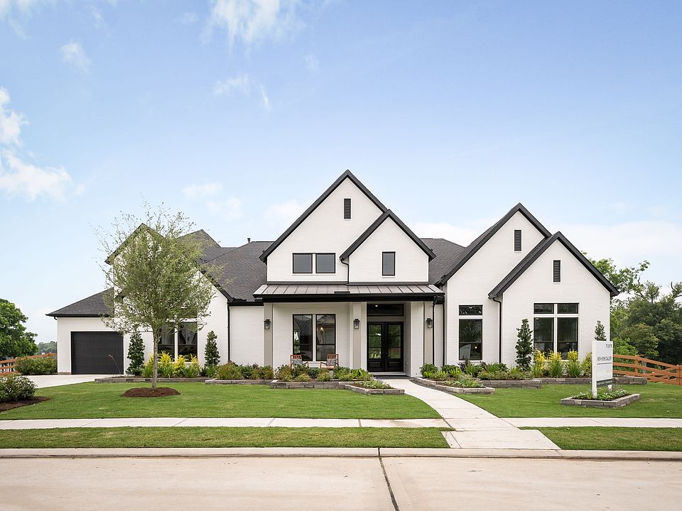 A large, modern farmhouse-style home with a prominent gabled roof and a well-manicured lawn and land