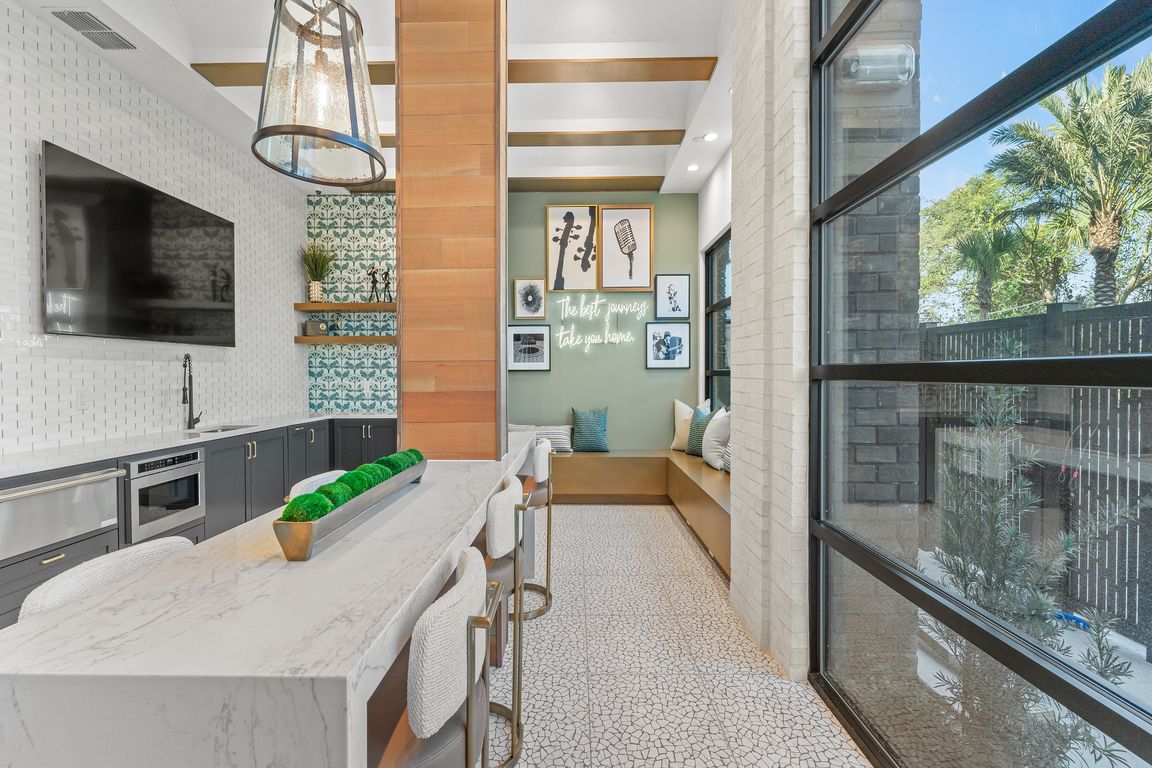 Chic modern kitchen with a stylish island, elegant lighting, and cozy seating area with a scenic view through large window.