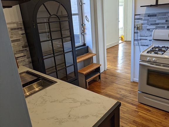 Another view of the newly remodeled kitchen, showing steps to roof deck. Kitchen has gas range, new fridge, new dishwasher, countertop, sink. Lots of cabinet, pantry, and shelf space, marbled backsplashes at sink and range.
