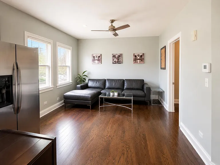 Open living area with hardwood floors, large windows, and a sectional seating setup next to the kitchen.