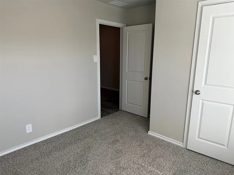 Light gray wall with white baseboards, featuring two white interior doors with chrome hardware, and gray carpeting