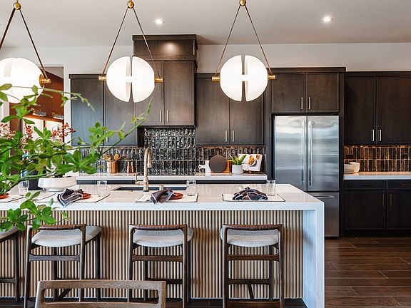 A modern and stylish kitchen with a large island, dark cabinets, and pendant lights, surrounded by p