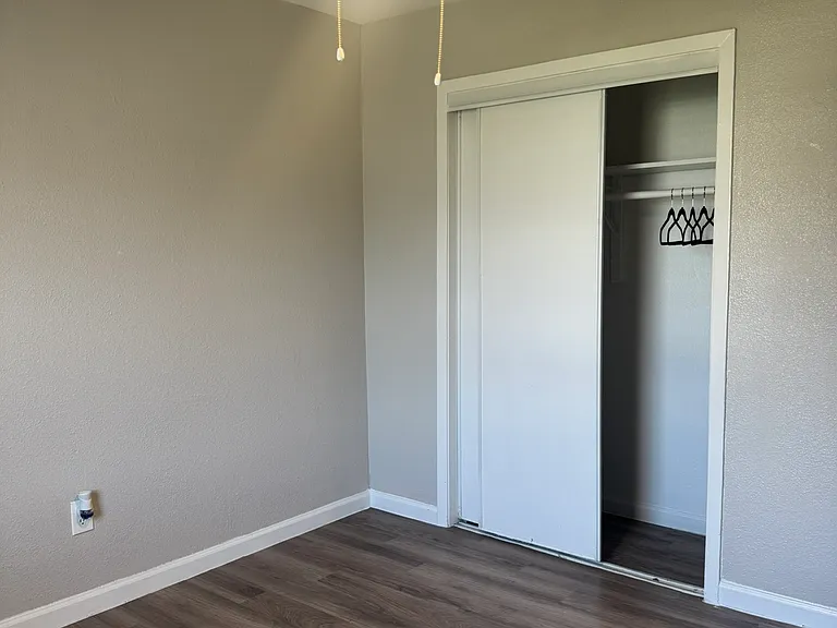 This cozy bedroom features fresh neutral paint, wood_style flooring, and a modern ceiling fan with a convenient sliding_door closet.