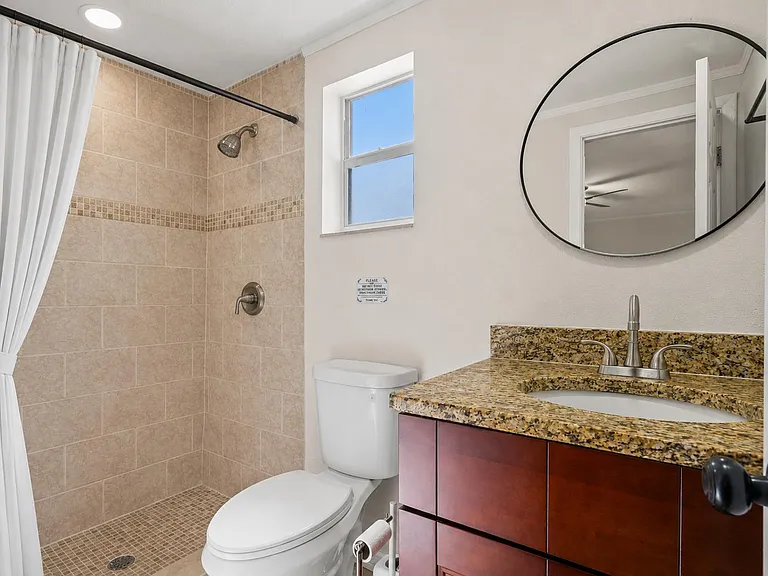 Full bathroom with tiled walk-in shower, granite vanity, and window for natural light and ventilation.