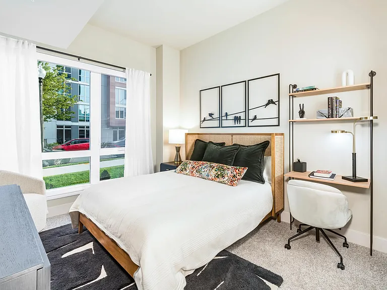 This bright and thoughtfully designed bedroom features plush carpeting, natural light, and a built-in workspace to help you recharge and refocus.