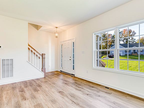 Bright, empty room in Poplar Village s Lot 29 with wood floors, large window, staircase, and abundan