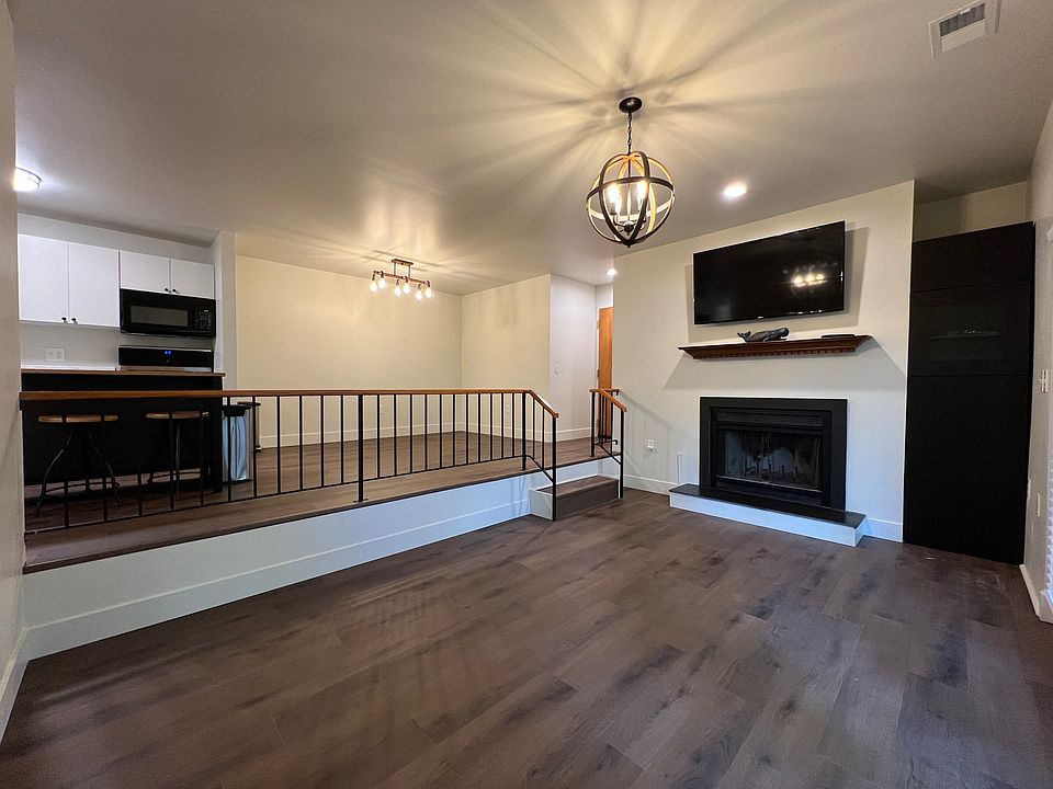 Open concept view from living room into dinning and kitchen. Cozy living room with fireplace, sleek slate stone hearth, built-in cabinet with concealed cabling, and entry to a charming covered patio to the right.