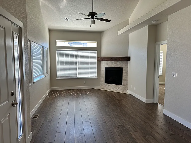 Living room with gas fireplace, vault ceiling, ceiling fan and window coverings. Master bed and bath to the right.