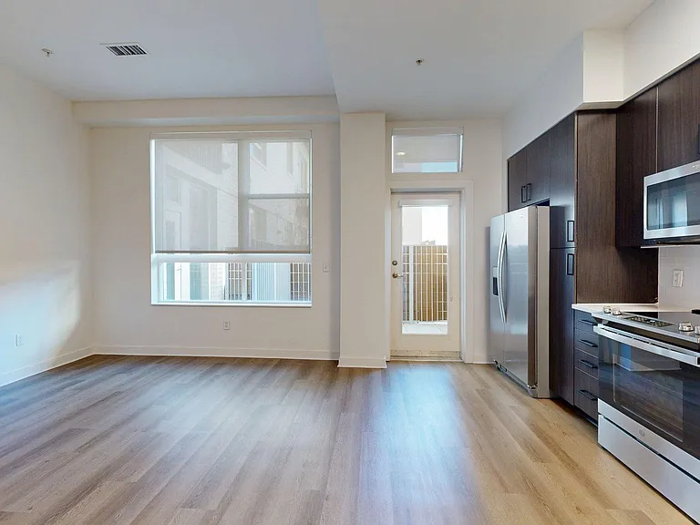 Apartment kitchen with stainless steel appliances, dining and living room with wood-style flooring.