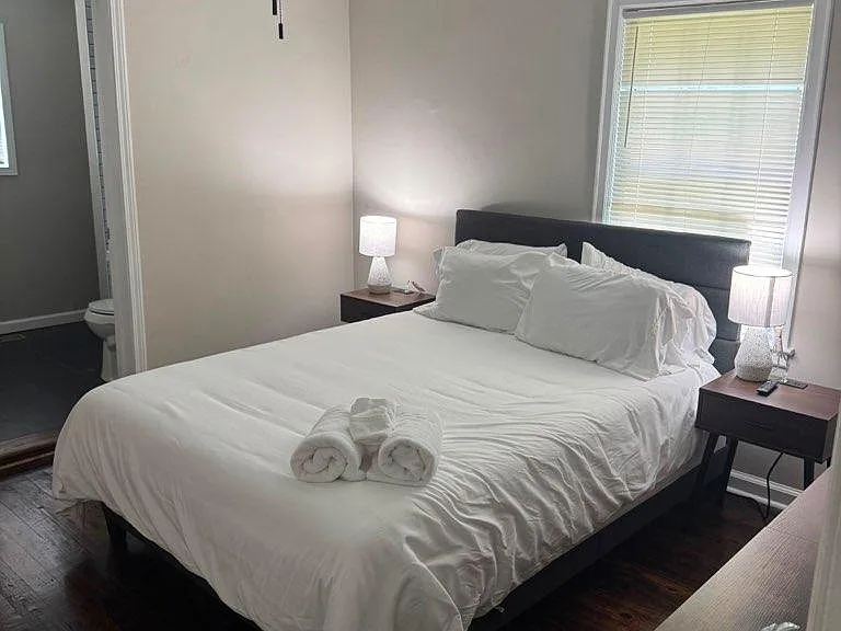 Comfortable bedroom with a ceiling fan, hardwood floors, and a window with blinds, plus nightstands for bedside storage.