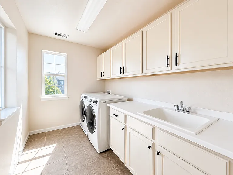 Second-floor laundry room with full-size washer and dryer, utility sink, counter space and extensive storage. Digitally enhanced for presentation.