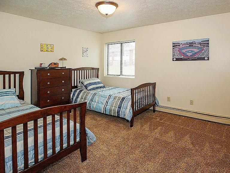 Inviting bedroom with twin beds, stylish wooden furniture, and soft carpet flooring, perfect for comfort and relaxation.