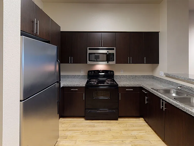 Apartment kitchen with granite countertops, dark wooden cabinets, and hardwood floors.