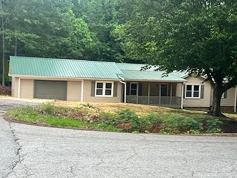 EXTERIOR FRONT VIEW WITH METAL ROOF AND LARGE COVERED FRONT PORCH. SOME SHADE TREES IN THE FRONT