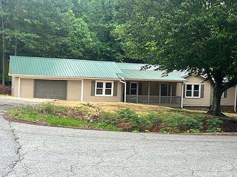 EXTERIOR FRONT VIEW WITH METAL ROOF AND LARGE COVERED FRONT PORCH. SOME SHADE TREES IN THE FRONT