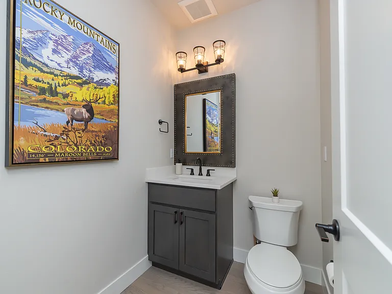 Stylish main-level powder bath featuring designer lighting, matte black fixtures, and a rustic-chic mirror for a warm mountain touch.