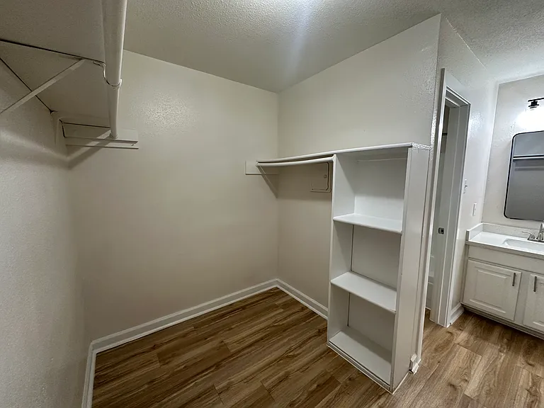Spacious walk-in closet with sleek flooring, built-in shelving, and convenient access to a modern bathroom. Spacious walk-in closet with sleek flooring, built-in shelving, and convenient access to a modern bathroom.