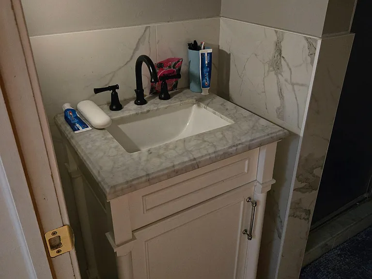 Bathroom vanity with a stone-look countertop, undermount sink, and matte black faucet with cabinet storage below.