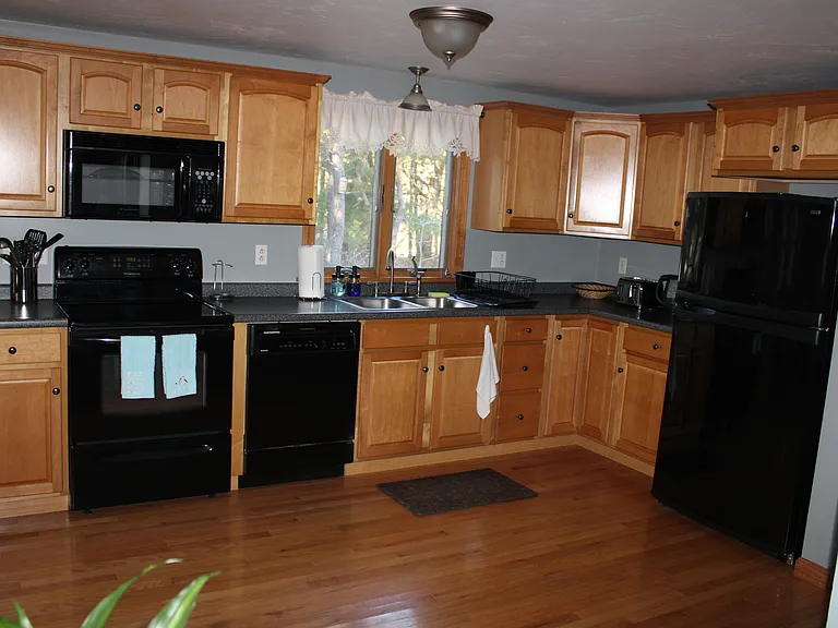 Well_kept first_floor kitchen with stove, microwave, refrigerator, sink, coffee maker, and kettle. Clean, naturally lit shared space ideal for simple meal prep.