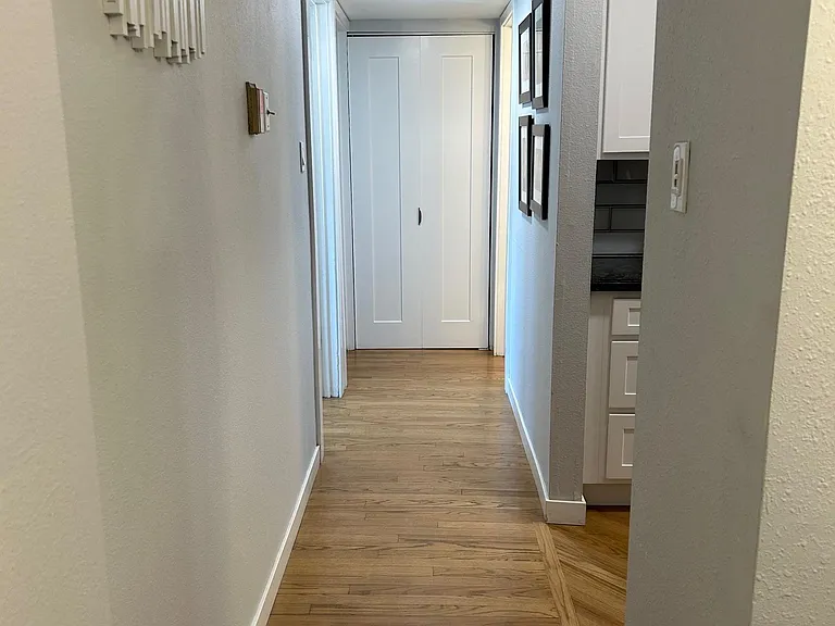 hall way from living room connecting bedrooms. To the right is a walk through kitchen and storage closet at the end of the hallway