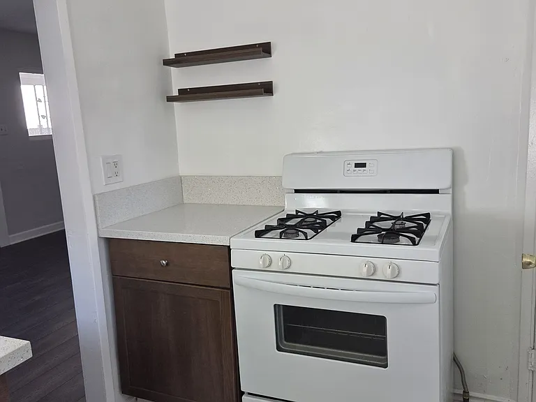 Kitchen with newly installed cabinets and counter top also includes small shelving for spices, a white refrigerator and stove.