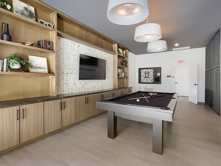 Game on. The Garrett Uptown billiards room features a sleek pool table, wall-to-wall brass shelving, terrazzo accent wall, and board games _ your go-to hangout spot.