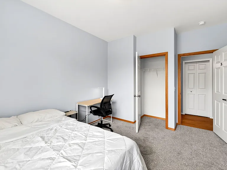 Private bedroom with carpet flooring, a work desk setup, and a walk-in closet for convenient storage near the entry.