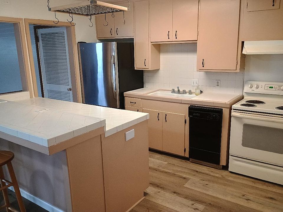 Tiled kitchen with stainless steel refrigerator, electric stove, small dishwasher, breakfast bar.
