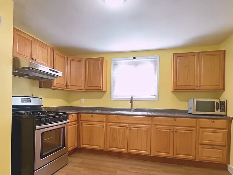 Overview of the kitchen featuring furnished cabinets, an industrial-grade microwave and a new gas range. A large refrigerator is included with the space, though it is not shown in the picture.