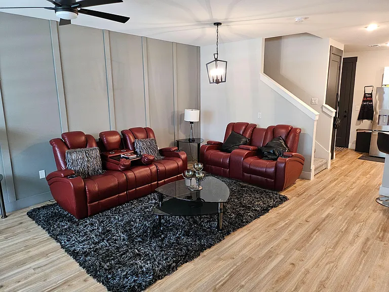 Spacious living room with plush seating, ceiling fan, and durable wood-look flooring, flowing into the adjacent kitchen.