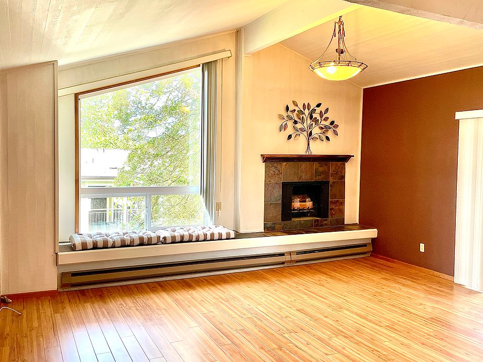 Open living room with a high ceiling, bay window and wood fireplace.