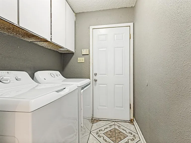 Dedicated laundry area with side-by-side washer and dryer, plus overhead cabinetry for detergent and linen storage.