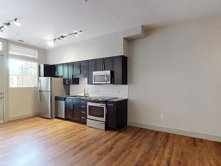 Apartment kitchen with stainless steel appliances, dining and living room with wood-style flooring.