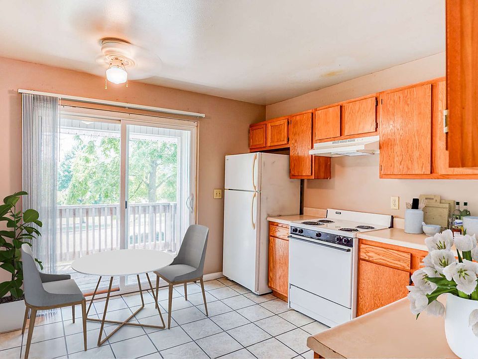 A simple kitchen with wooden cabinets, a white refrigerator, stove, microwave, and dishwasher on tiled flooring.