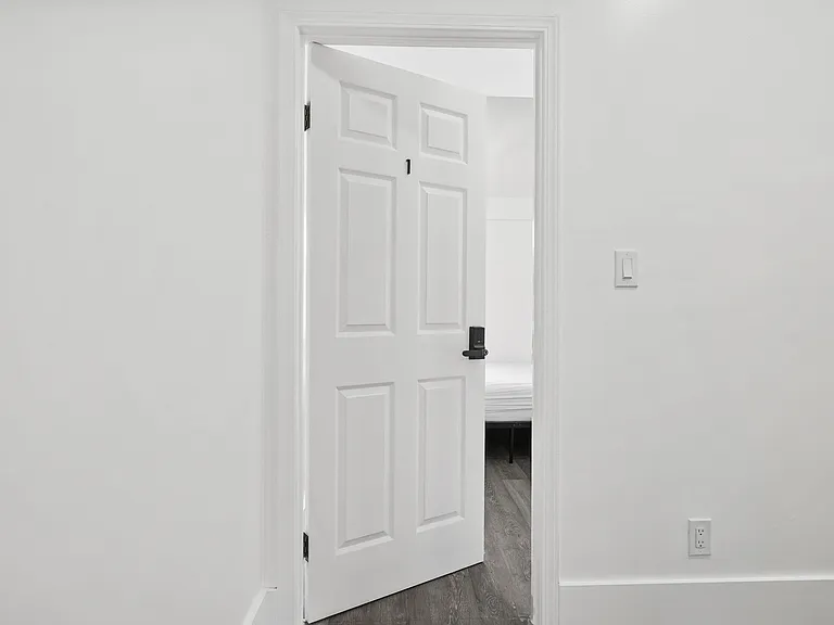 Entry hallway with fresh white walls, paneled door, and durable wood-look flooring leading into the bedroom.